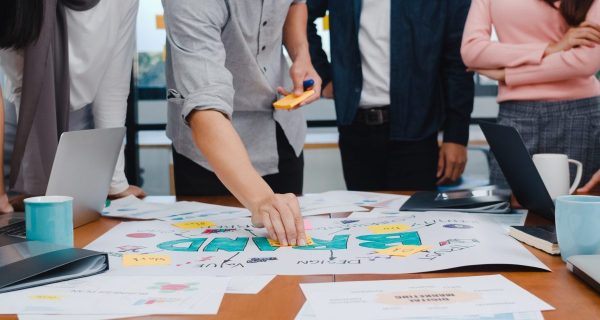 Happy young Asian businessmen and businesswomen meeting brainstorming ideas about new paperwork project colleagues working together planning success strategy enjoy teamwork in small modern office.
